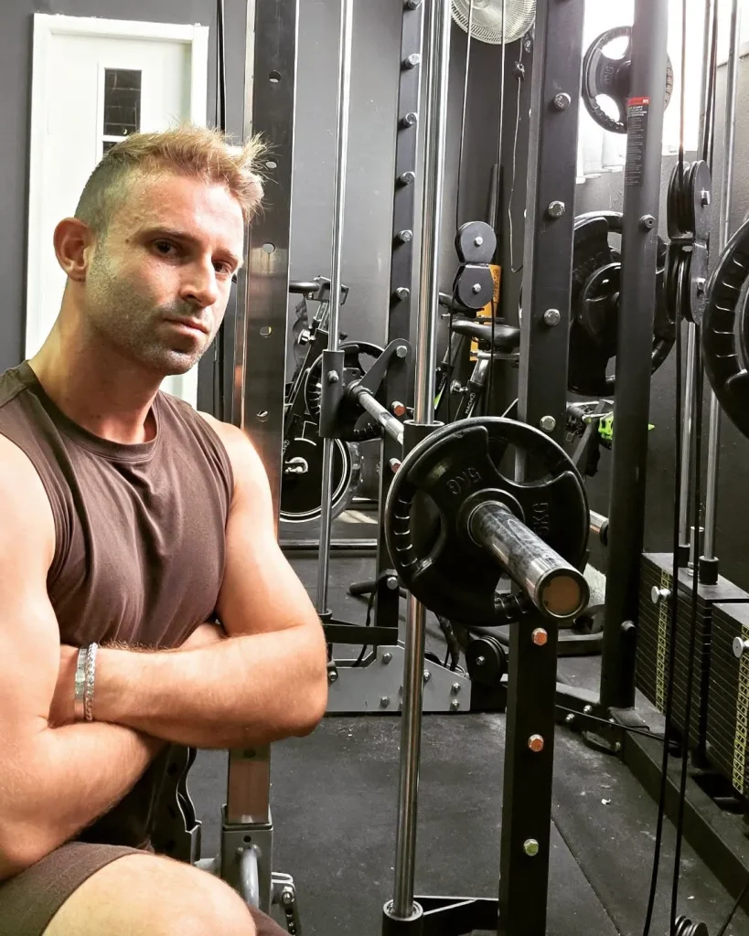 אנטון טל יושב בחדר כושר, ידיים שלובות, מביט למצלמה